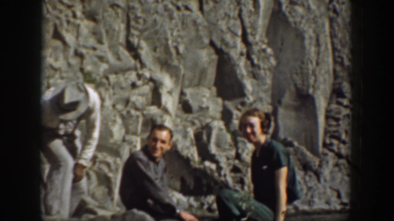 Three adults seated near a rocky cliff face during an outdoor picnic scene.