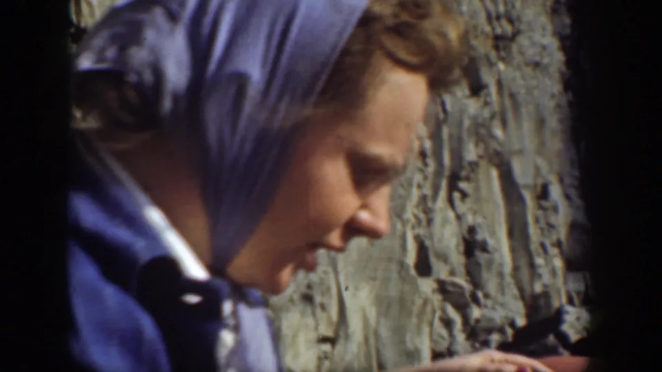 Close 1937 California frame of a woman in a blue headscarf near a textured rock face during the outdoor picnic.