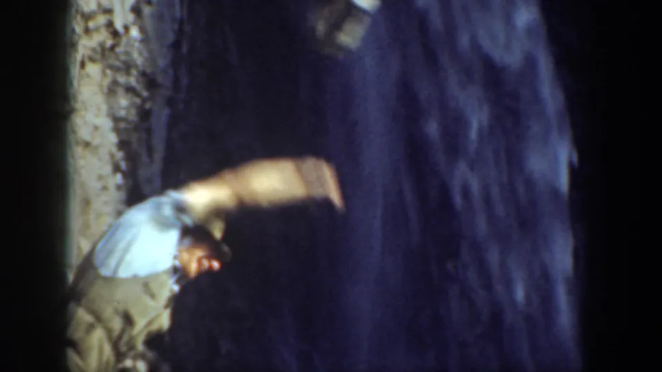 1937 California home-movie frame of a man bending near a cliff face and dark waterfall, partly blurred by motion.