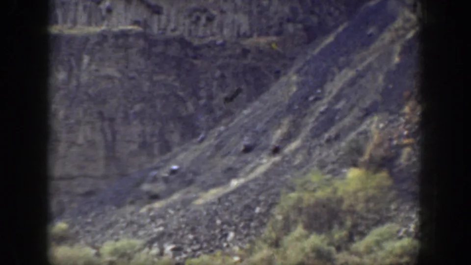 1937 California 8mm frame showing a rocky slope, cliff wall, loose stones, and sparse vegetation in a rugged outdoor setting.