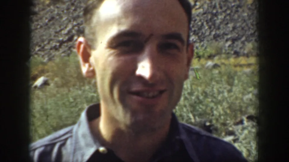 1937 California 8mm close-up of a smiling adult man with rocks and water behind him in the outdoor setting.