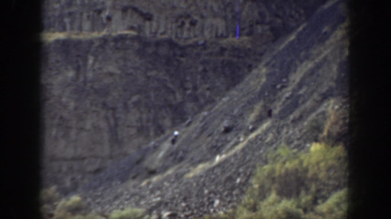 1937 California 8mm frame showing a distant hiker on a steep rocky slope below darker cliff formations.