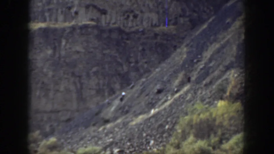 1937 California 8mm frame showing a distant hiker on a steep rocky slope below darker cliff formations.