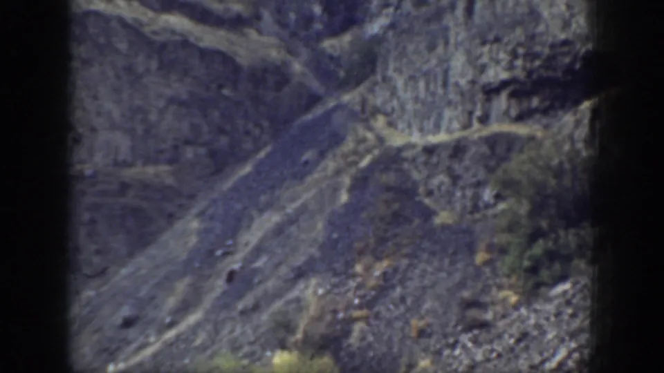 1937 California home-movie frame of a rugged mountainside, showing scree, layered rock, sparse shrubs, and pale diagonal traces.