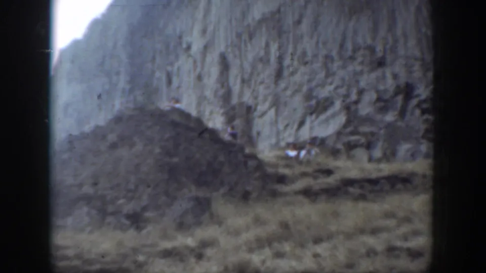 1937 California 8mm footage showing tiny hikers below a high rock face on a rugged mountain slope.