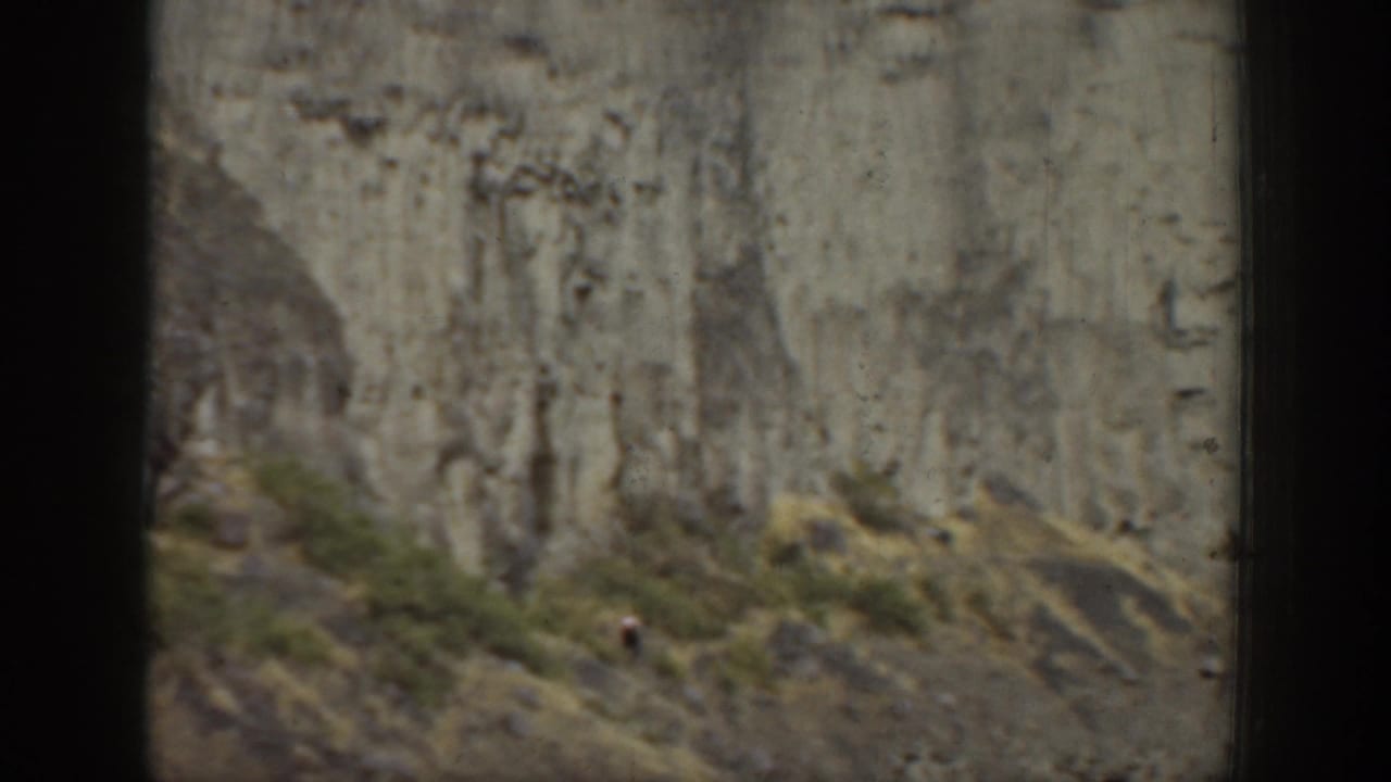 1937 California 8mm frame showing a small climber on a steep rock wall above scrubby terrain.