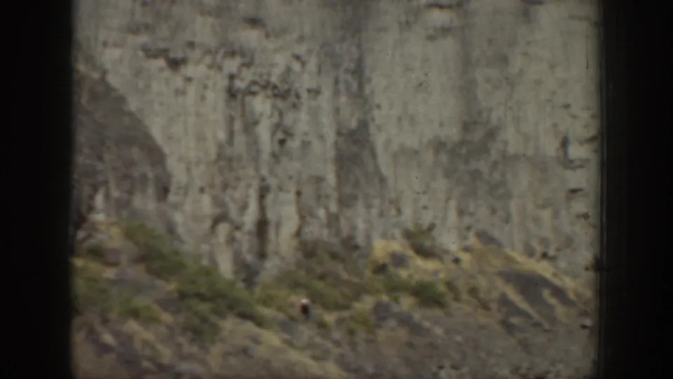 1937 California 8mm frame showing a small climber on a steep rock wall above scrubby terrain.