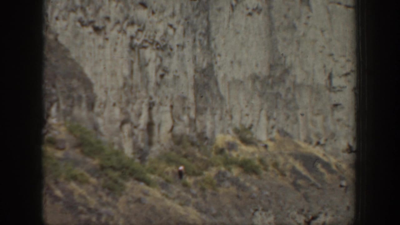 Rocky cliff and scrub hillside with a small figure near the slope.