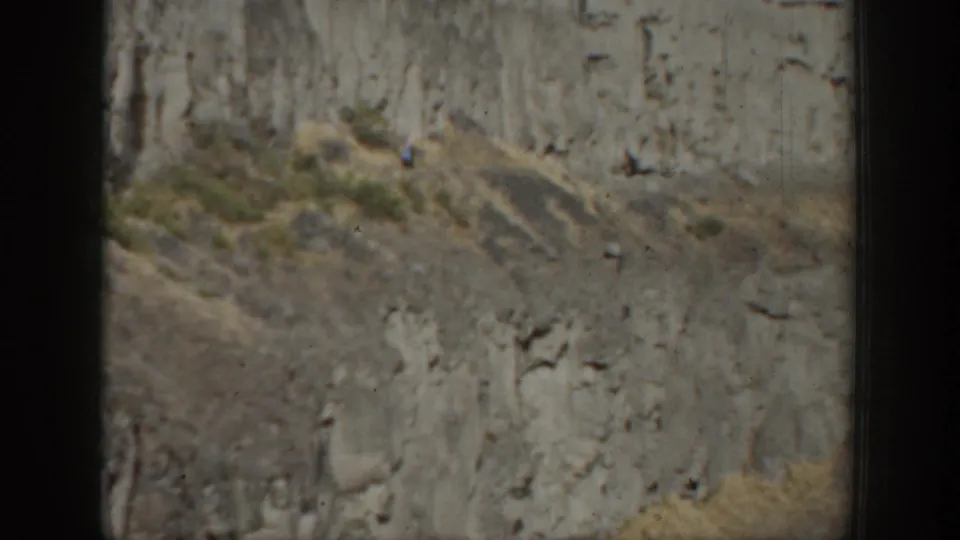 California 1937 8mm frame with a distant person on rugged cliff terrain and sparse vegetation.