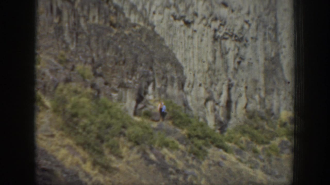 1937 California 8mm frame showing a woman at distance on a steep trail beneath rugged vertical rock formations.