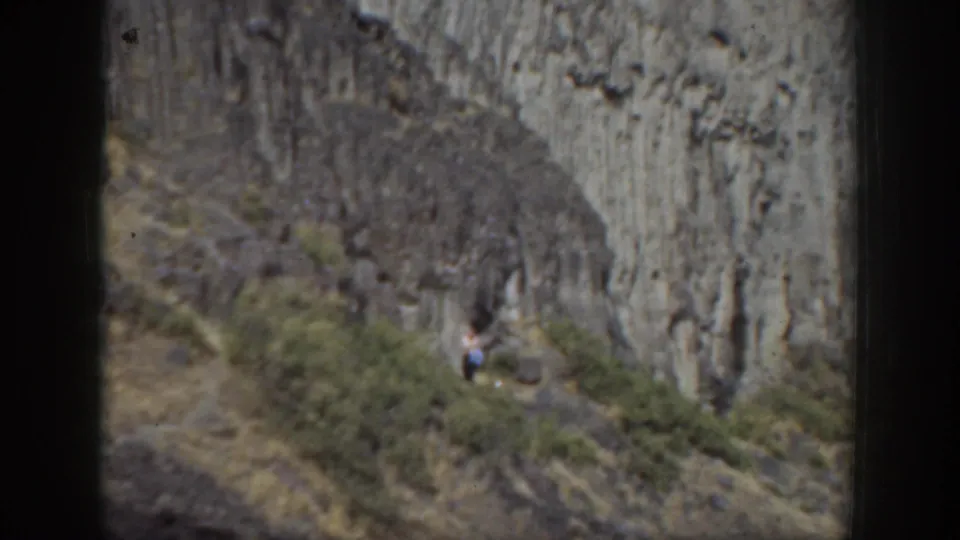 1937 California 8mm still showing a woman carefully descending a rugged hillside trail beneath a weathered rock face.