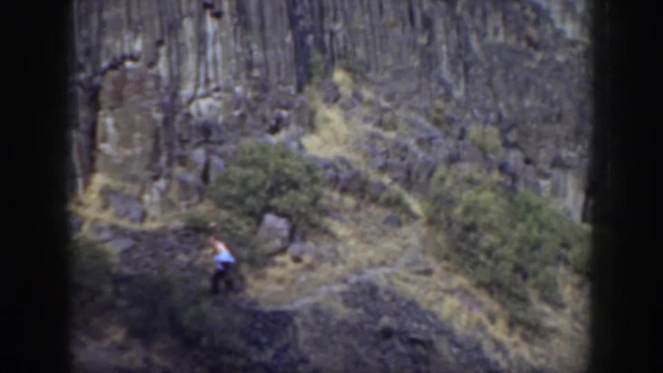 A distant hiker walks along a narrow California hillside trail beneath tall rock columns in 1937 home-movie footage.