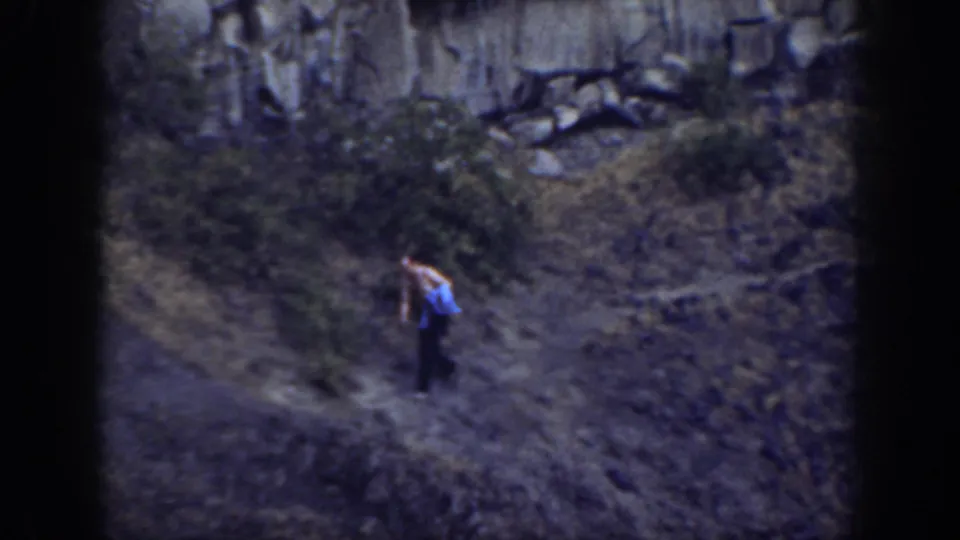 A lone hiker continues along a faint trail across a rugged grassy California slope in soft 8mm color footage.