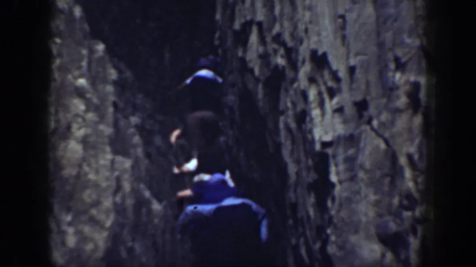 Home-movie frame from 1937 California showing people moving upward through a tight rocky passage.