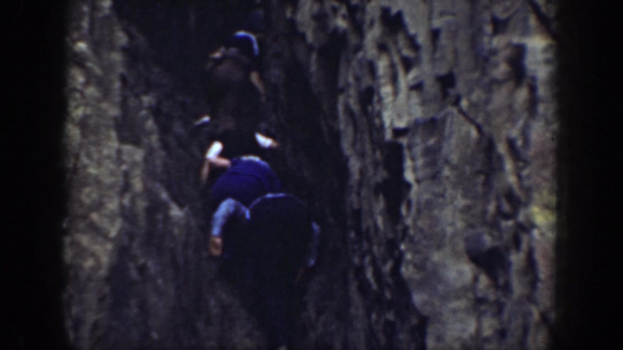 Two figures appear in a tight California rock passage, with one wearing a light hat and another lower in a blue shirt.