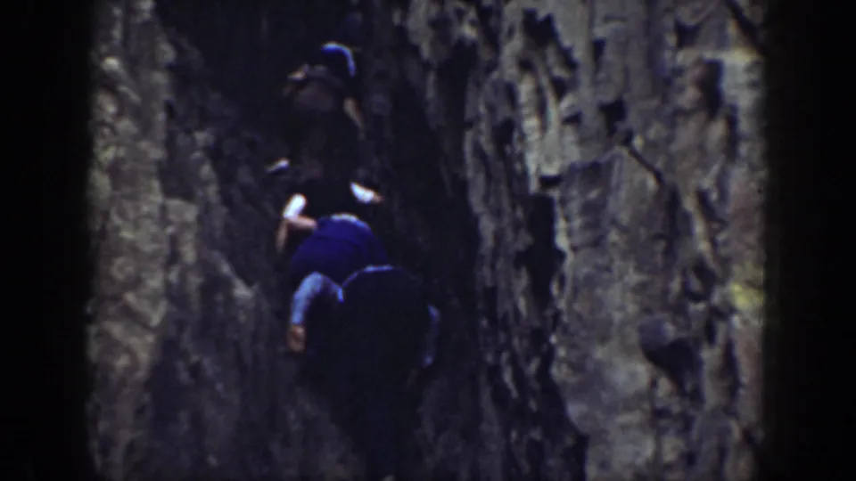 Two figures appear in a tight California rock passage, with one wearing a light hat and another lower in a blue shirt.