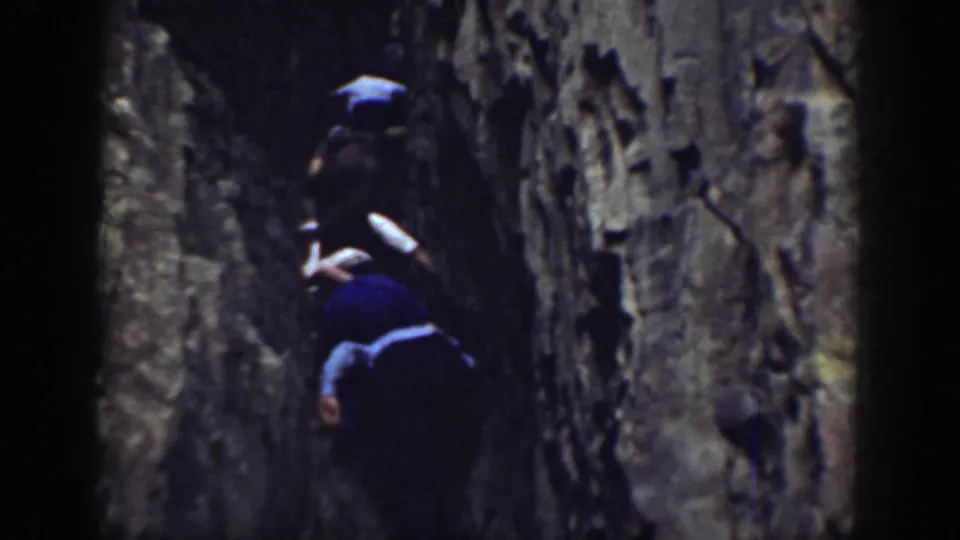 The 8mm frame shows climbers partly obscured by shadow as they pass through a narrow rocky slot.