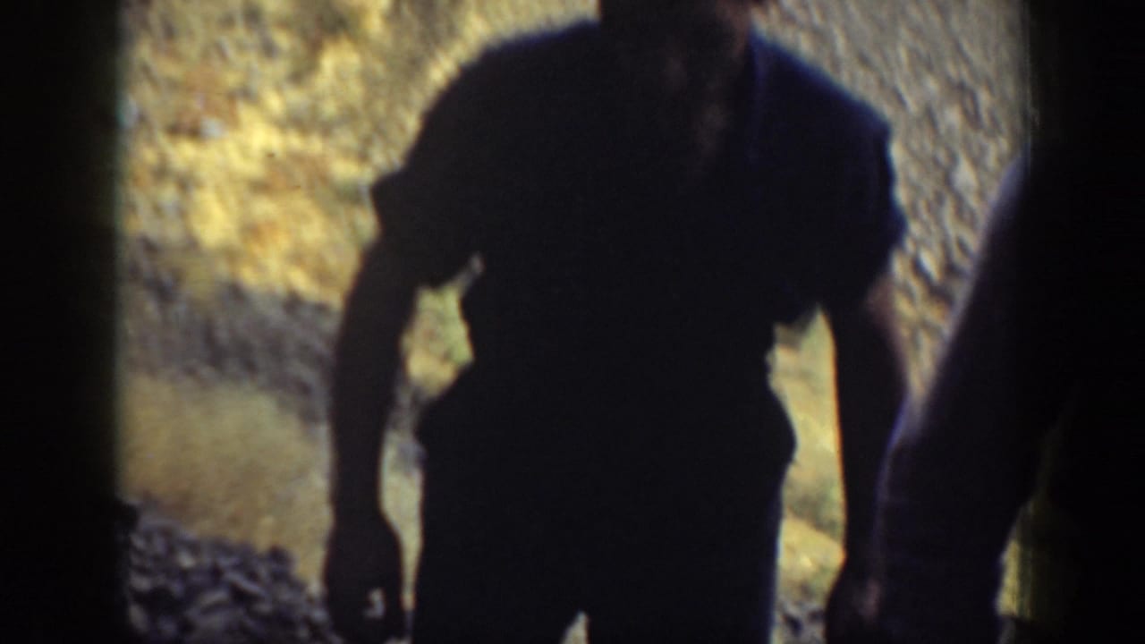 Adult men appear close to the camera in an arid California landscape, with soft focus and dark gate edges.
