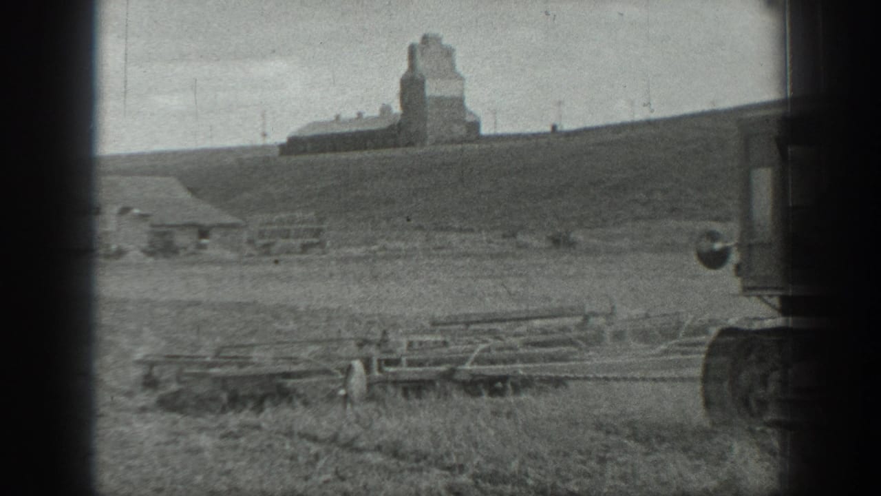Black-and-white 1937 California rural field view with a distant grain elevator and foreground farm structures partly obscured by film-edge shadow.