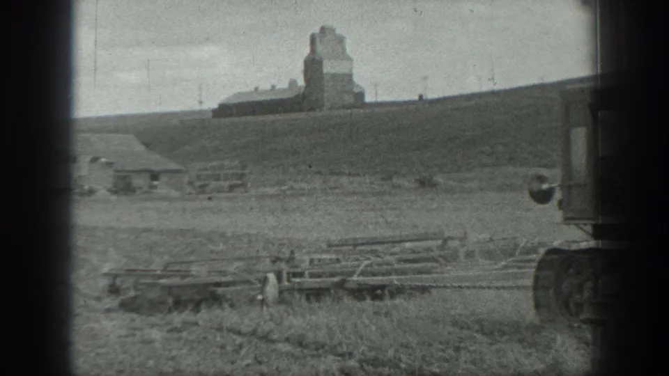 Black-and-white 1937 California rural field view with a distant grain elevator and foreground farm structures partly obscured by film-edge shadow.