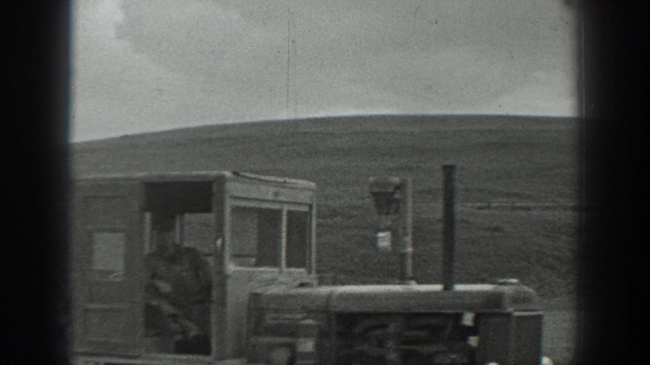 Man seated or standing at a vintage tractor in an open field.