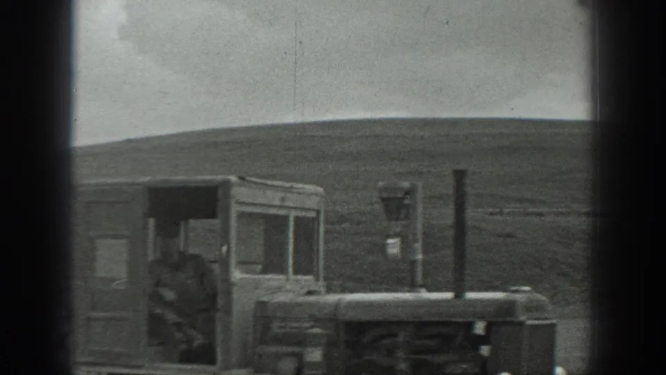 Man on a vintage tractor in a rural California field, with rolling land behind him and strong 8mm gate shadows at the frame edges.