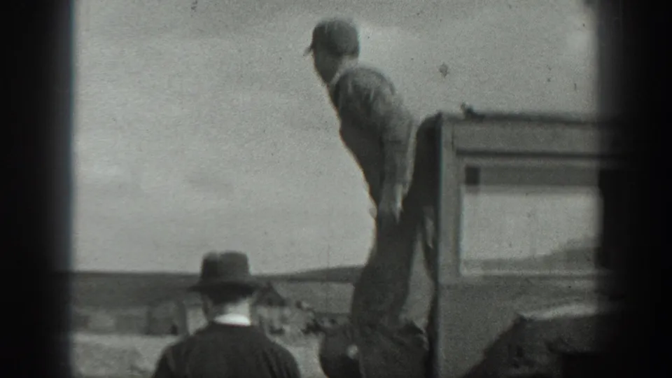 A farm worker stands on or beside the tractor in the 1937 California field scene, with a second hat-wearing person partly visible near the lower frame.