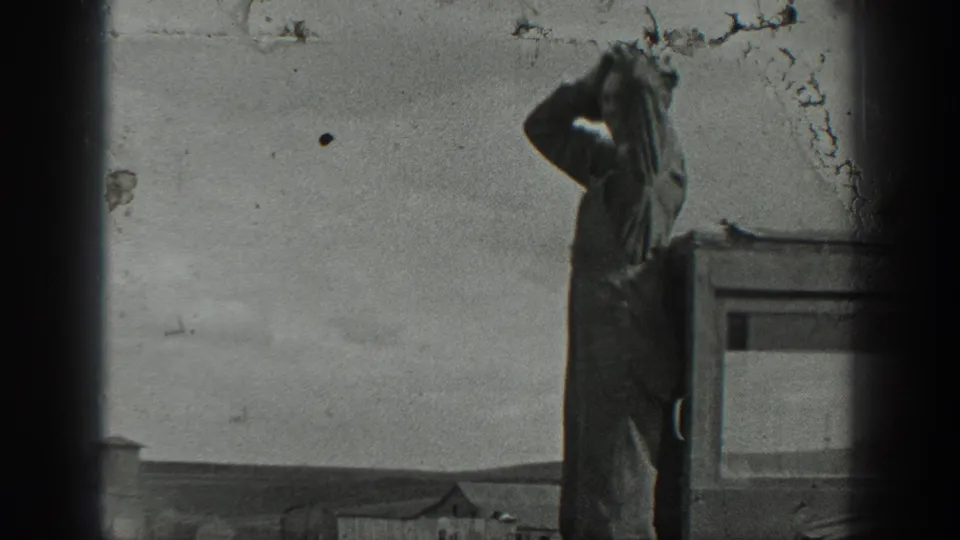 Man in work clothes stands on the tractor platform in rural California, shielding his eyes as he looks into the distance under an open sky.