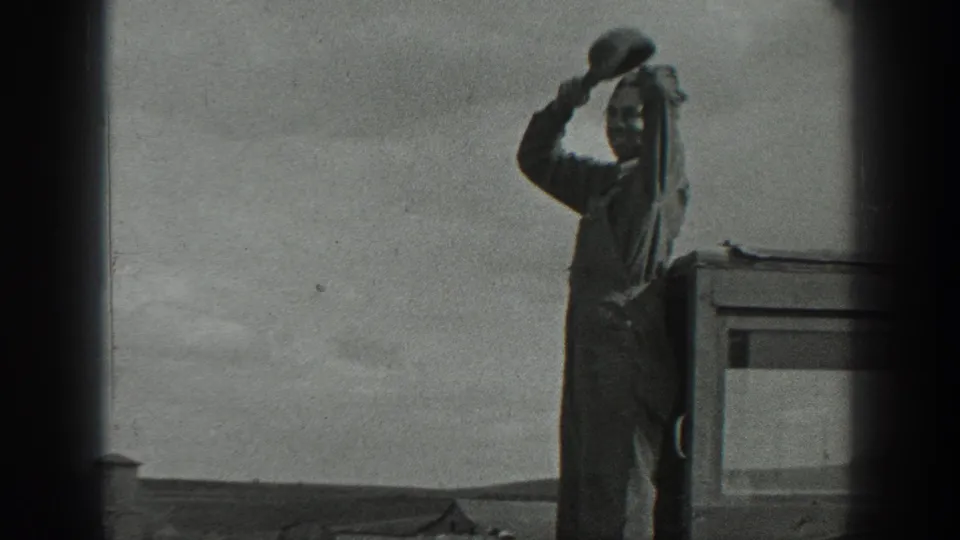 1937 California 8mm frame showing a man in overalls on a raised exterior surface, holding a hat near his face as he looks outward.