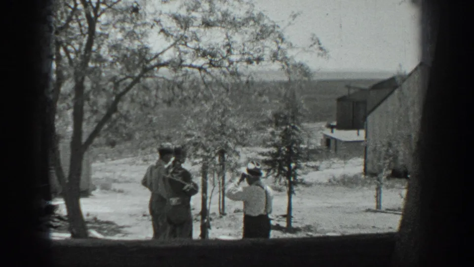 In this 1937 California 8mm frame, a person in a light shirt gestures toward two hat-wearing adults on a rural dirt road.