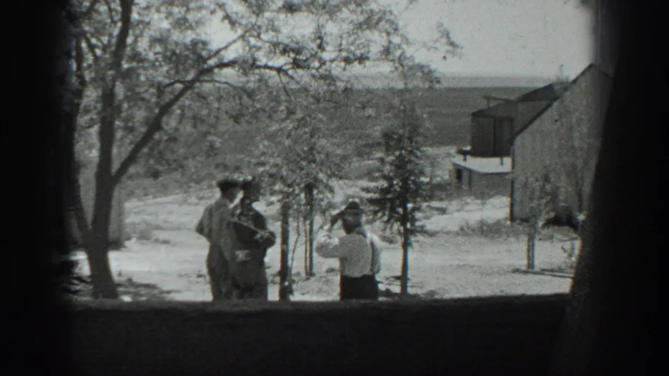 A window-framed 1937 California home-movie view shows men beside young trees, one appearing to hold a camera or similar object.