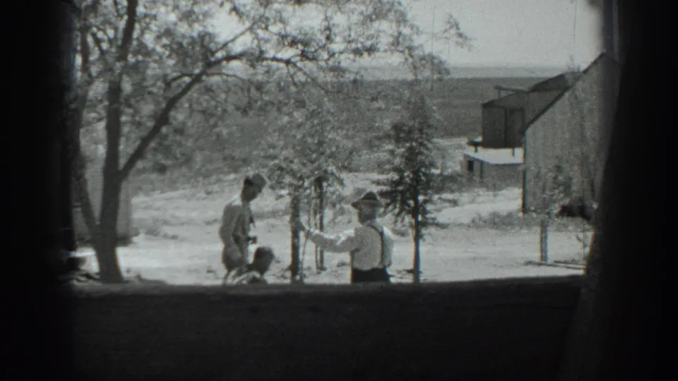 The final frame shows one man bending near the tree line as another in suspenders gestures, with a rural building and open fields beyond.