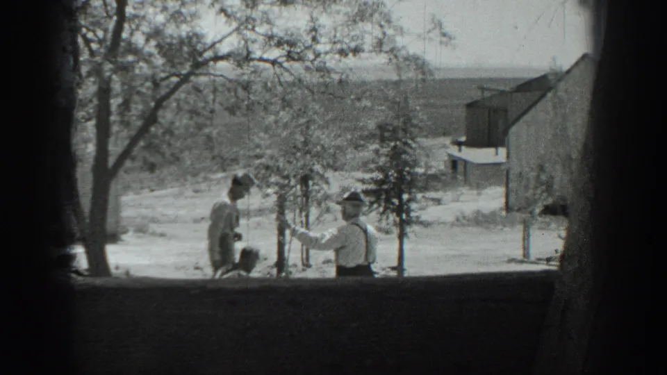 1937 California 8mm frame showing two men outdoors near trees, open ground, and a small structure in a rural setting.