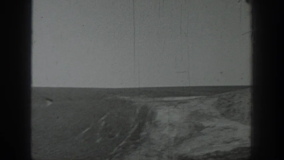1937 California 8mm frame showing open ground beside a low wall, with soft focus, scratches, and edge darkening.