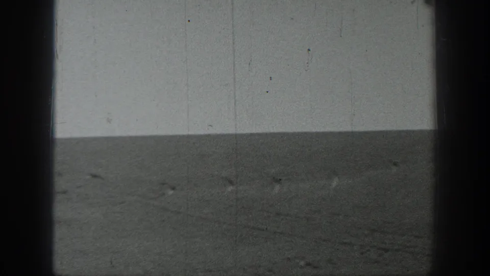Black-and-white 8mm view of an empty California landscape, with rough ground, a low horizon, and visible film scratches.