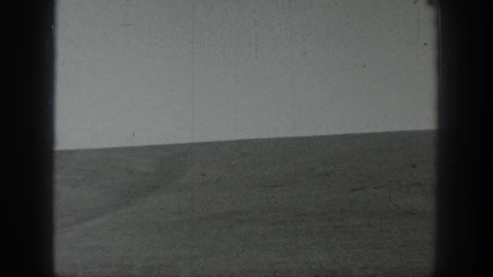 Final black-and-white 8mm frame of a broad California open landscape, with a flat horizon and worn film texture.