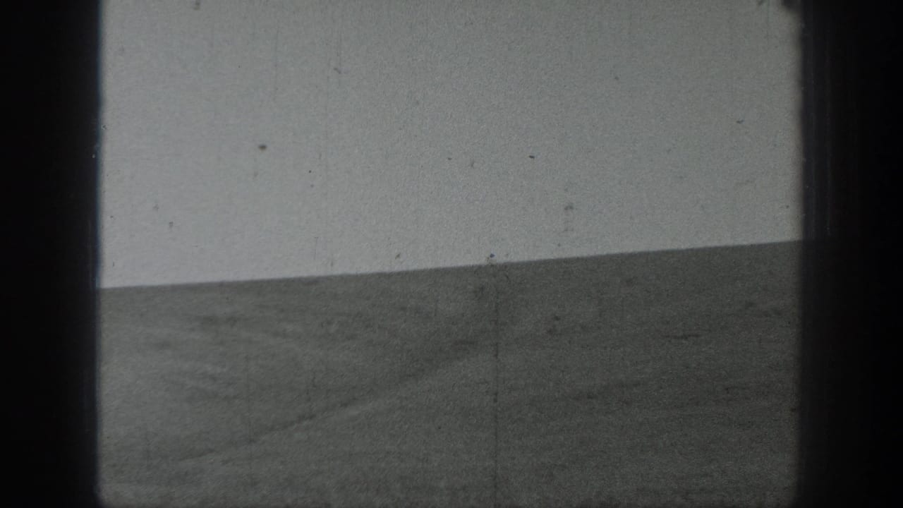 1937 California 8mm frame showing an open agricultural field, low hills, pale sky, and dark film borders during a pan.