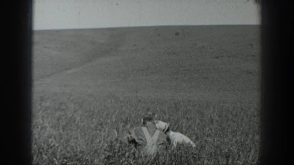 1937 California 8mm frame showing two distant field workers low among tall crops, with hats and open farmland behind them.