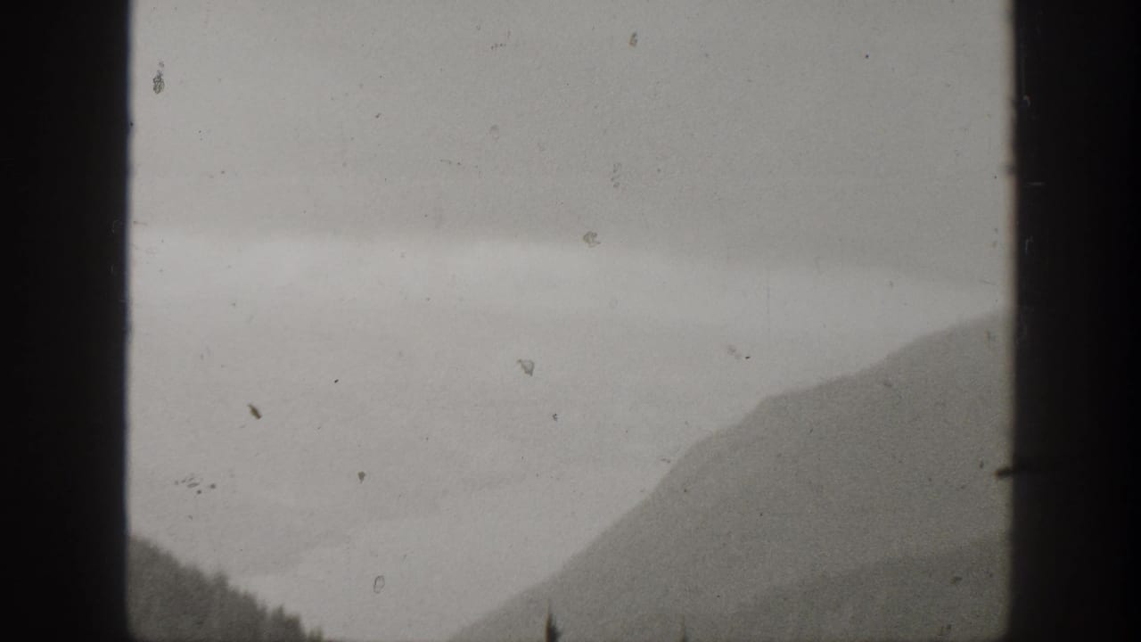 Fog-softened California mountain landscape from 1938 home-movie footage, with evergreen trees low in the frame and visible film wear.