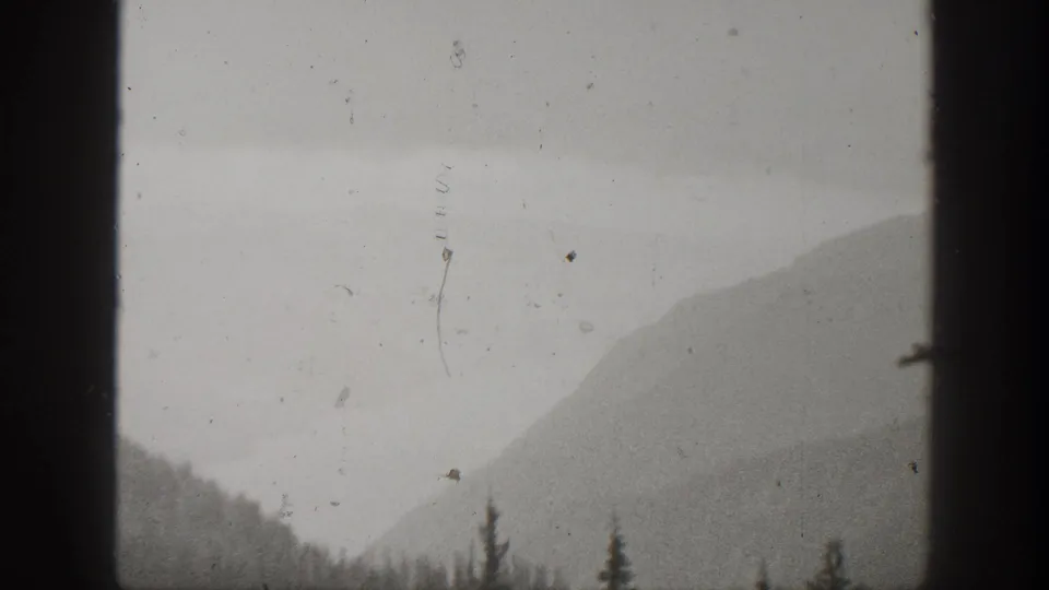A hazy mountain ridge in California appears through weathered 1938 8mm footage, with dark frame edges and sparse evergreen silhouettes.