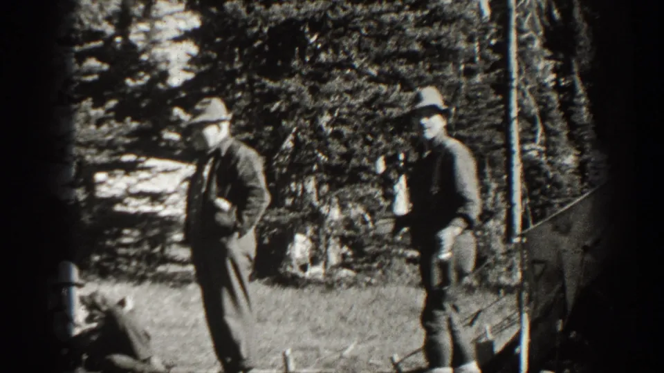 Two adult men in period outdoor clothing appear near evergreen trees in 1938 California home-movie footage, likely during a camping or hunting trip.