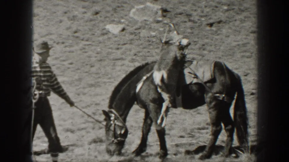 A man in a striped shirt leads a saddled horse across rocky California terrain in 1938 home-movie footage of an outdoor trip.
