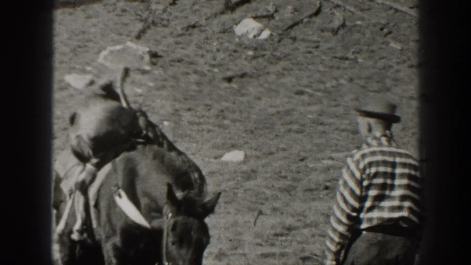 1938 California home-movie frame showing the pack mule and handler from behind in a dry, sparsely rocky landscape.