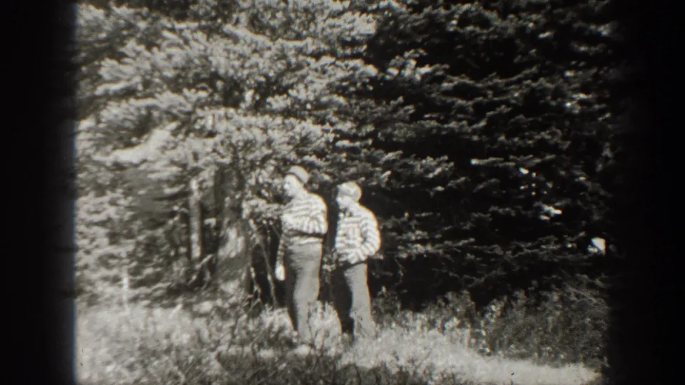 Two men in outdoor clothing stand by a wooded edge in the same 1938 California home-movie sequence.