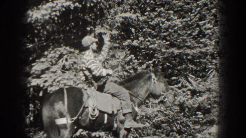 In California 1938 home-movie footage, an adult man in a cap and striped shirt sits on a saddled horse in a wooded area.