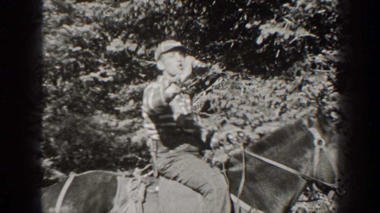 Young man in a cap drinks from a bottle while seated on a horse in a wooded area.