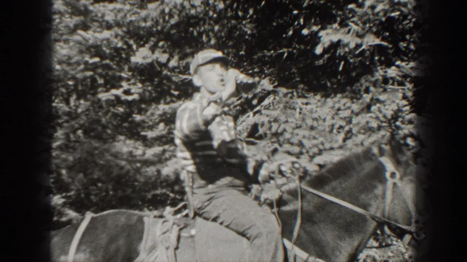 In 1938 California home-movie footage, a young man in a cap and striped shirt drinks from a bottle while riding a horse among trees.