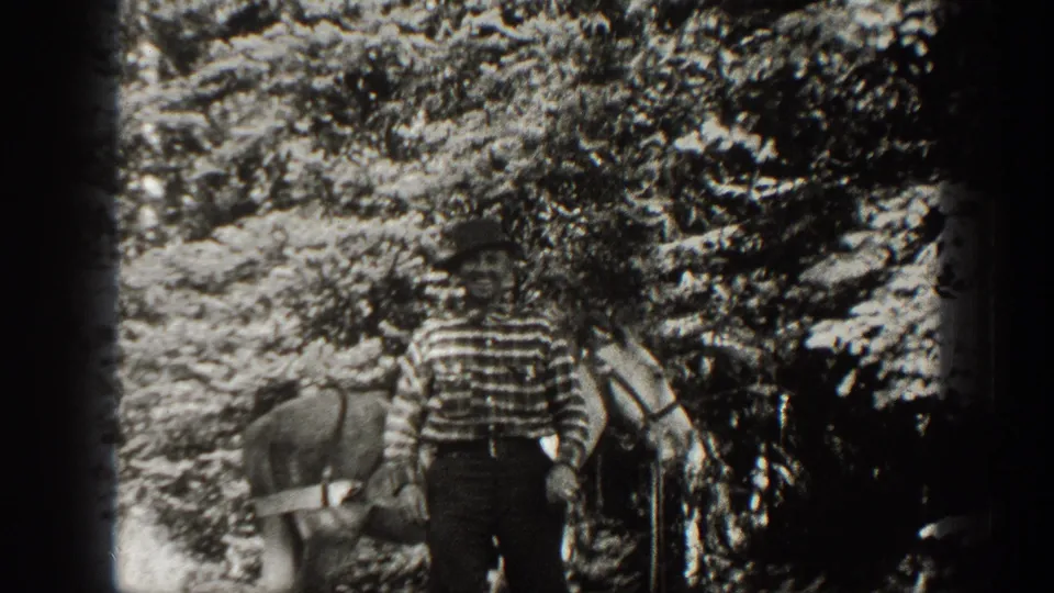 The rider in a striped shirt stands near the horse beneath trees in a high-contrast 1938 California home-movie frame.