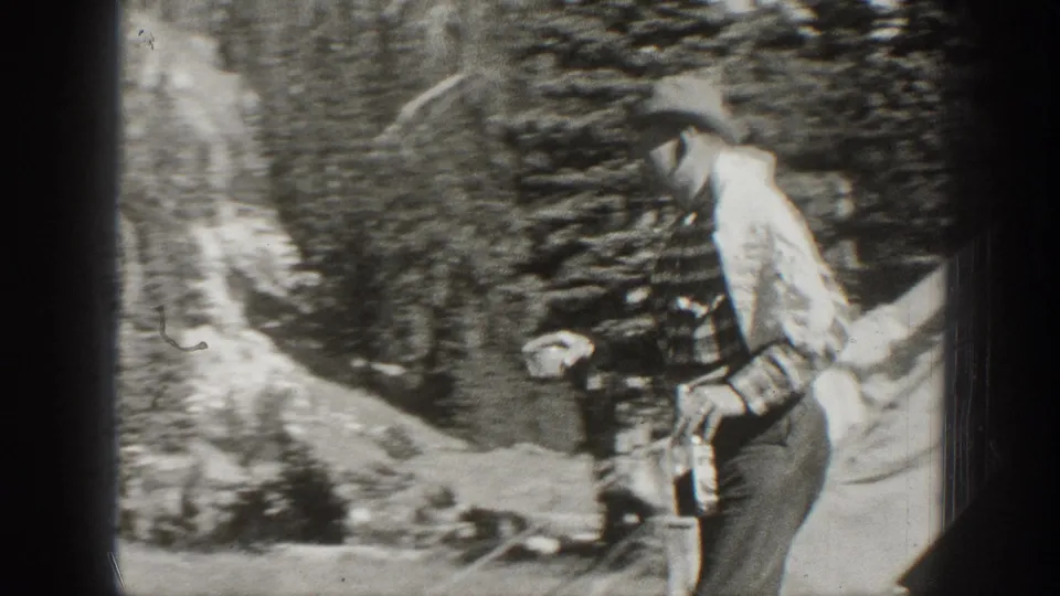 In 1938 California home-movie footage, a man in a striped shirt and brimmed hat walks through trees carrying a bottle.