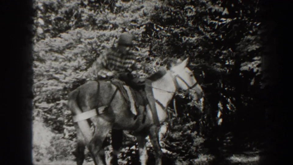 Black-and-white 1938 California home-movie frame showing a man in a striped shirt seated on a saddled horse among trees.